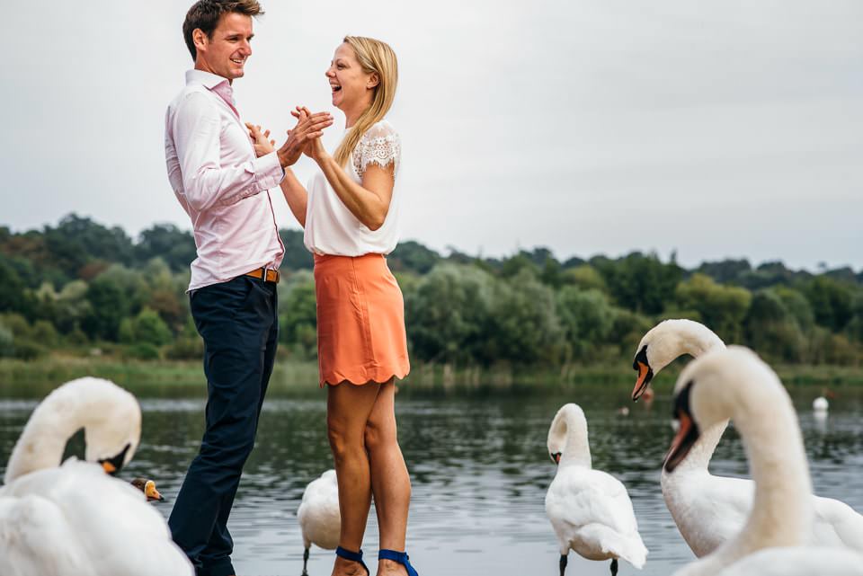 Two people holding each other being photographed surrounded by swans